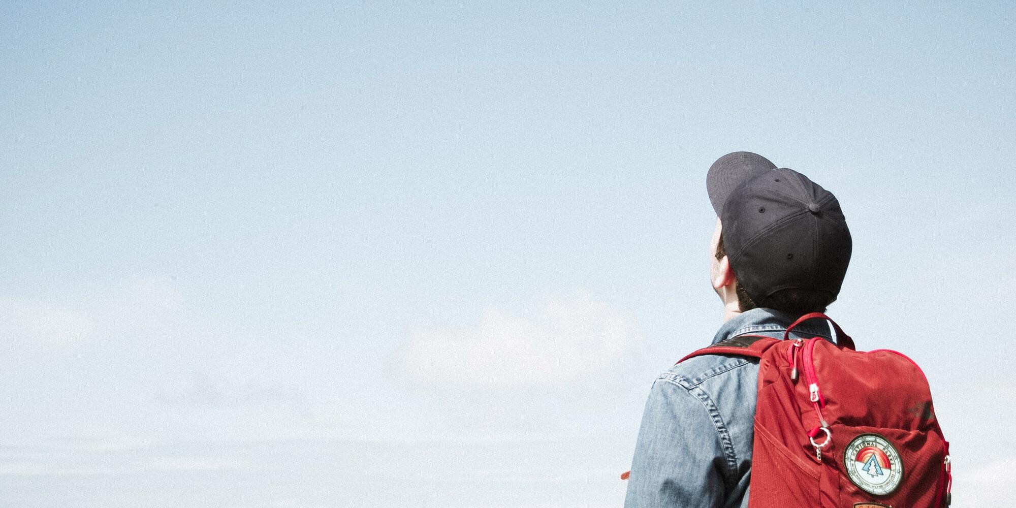 Mann mit Rucksack schaut in den Himmel